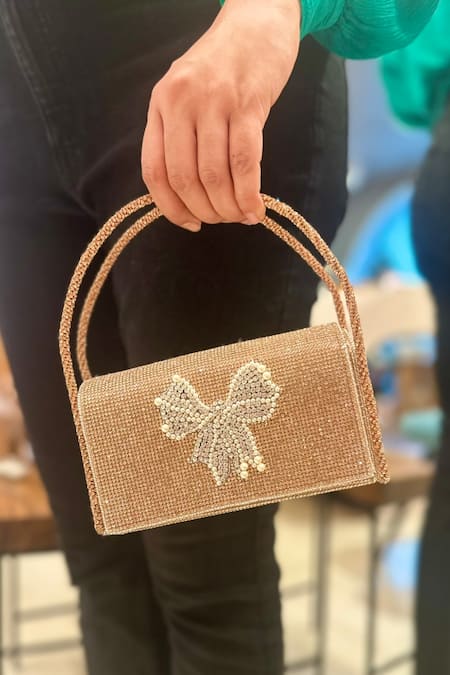 Ozel Rose Gold Crystal Bow Embellished Flap Bag at Aza Fashions Ozel_Rose Gold Crystal Bow Embellished Flap Bag _at_Aza_Fashions
